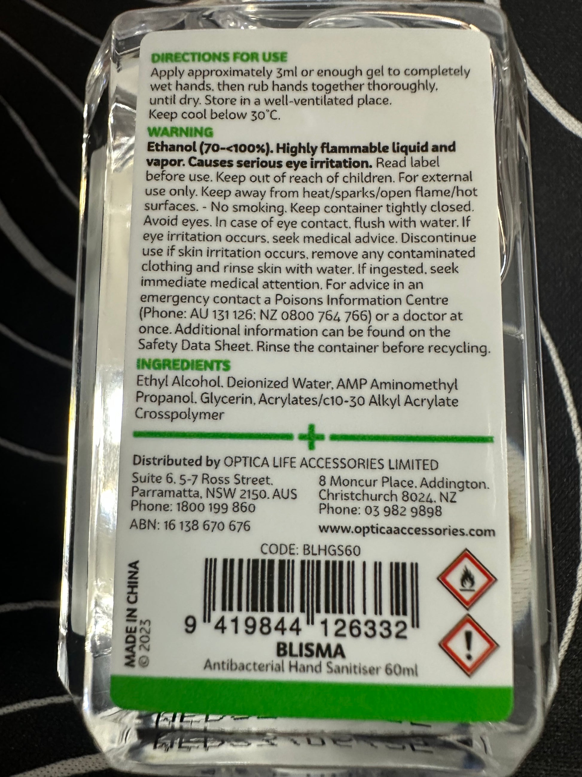 Back label of a small container with text and a barcode on a black and white striped background