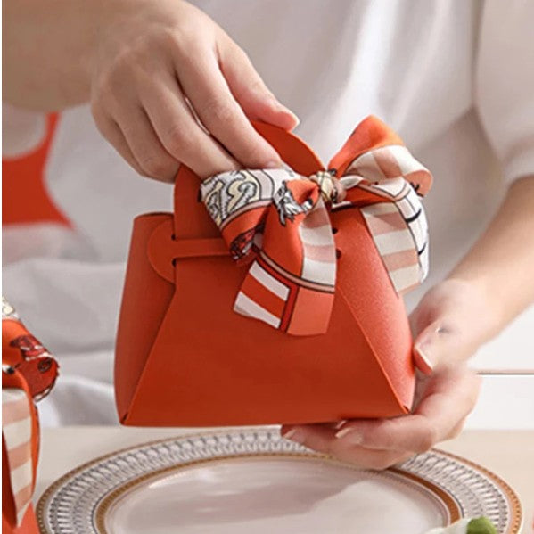 Person holding a small orange handbag with a decorative bow on a light background
