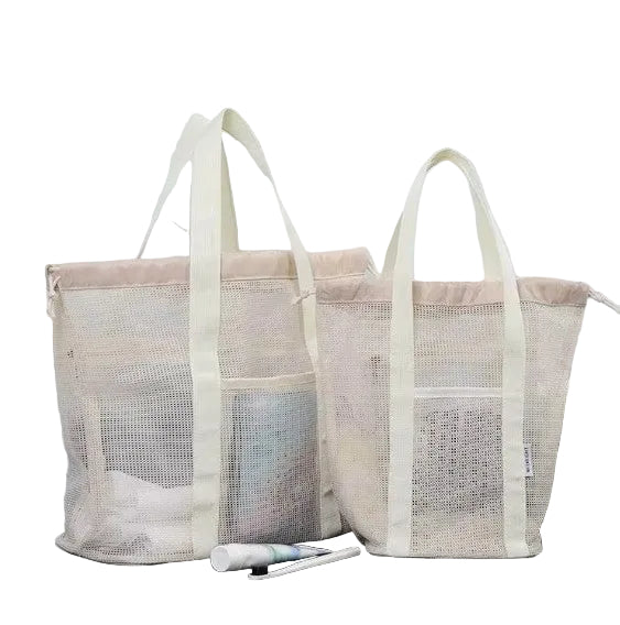 Two beige mesh laundry bags on a dark surface with a marble wall background.
